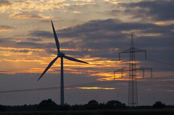 Wind power station and high voltage pylon in front of evening sky