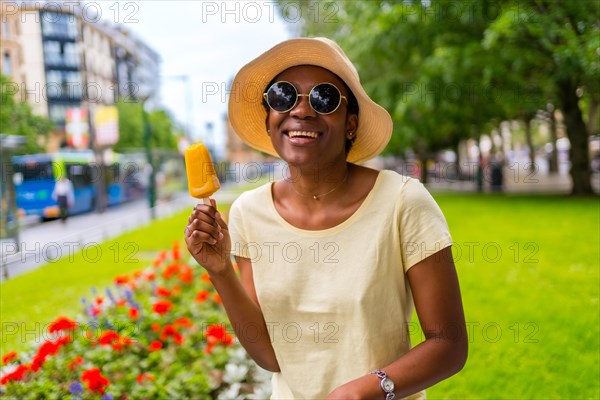 African black ethnicity woman eating a mango ice cream in the city in summer