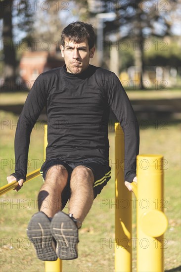 Fit young man doing push ups on horizontal bar outdoors