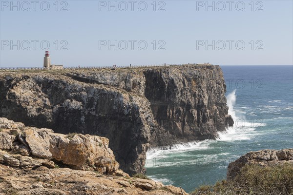 Surf on rocky cliffs in the Atlantic Ocean and the Farol de Sagres lighthouse on the site of the Fortaleza de Sagres fortress