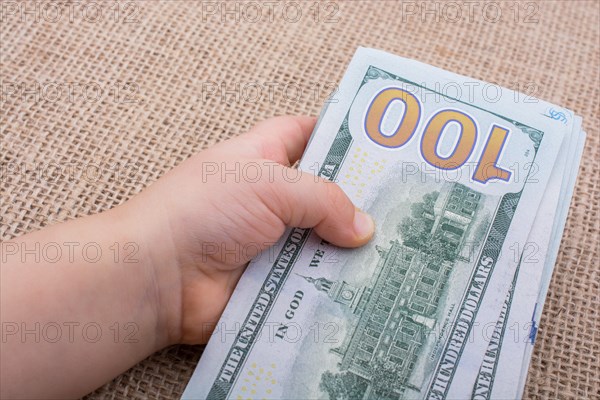 Toddler hand holding banknote bundle of US dollar on a linen canvas background