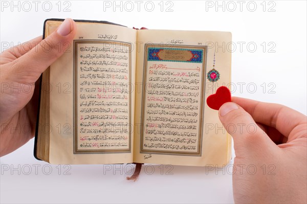 Hand holding The Holy Quran with a heart on a white background