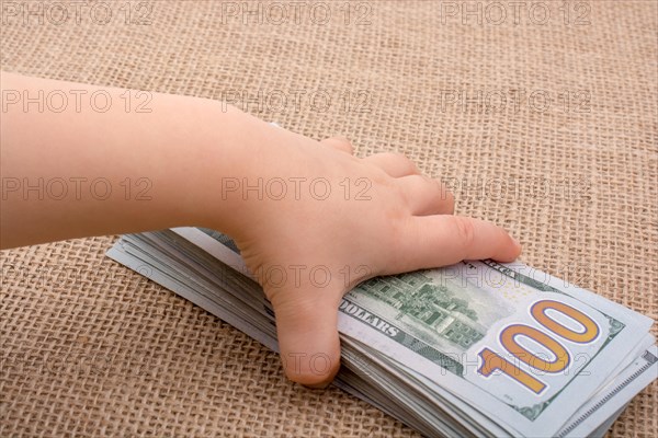 Toddler hand holding banknote bundle of US dollar on a linen canvas background