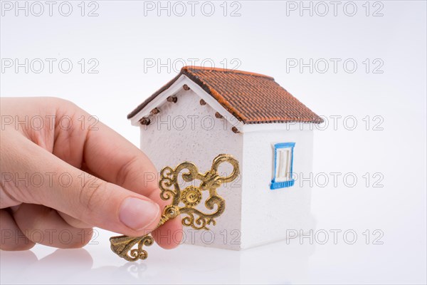 Hand holding a golden key near a house on a white background