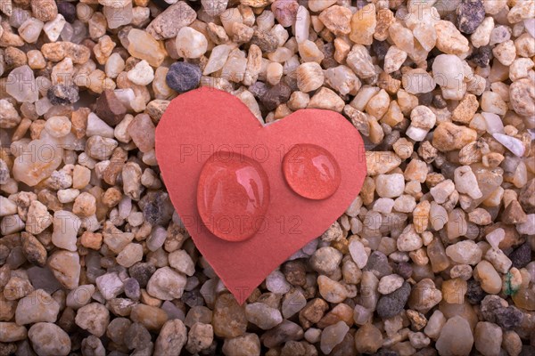 Water drops on a heart shaped paper on sand background