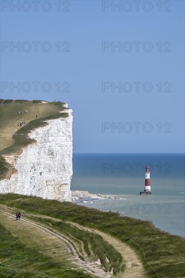 Tourists walking along the chalk cliffs overlooking Beachy Head lighthouse