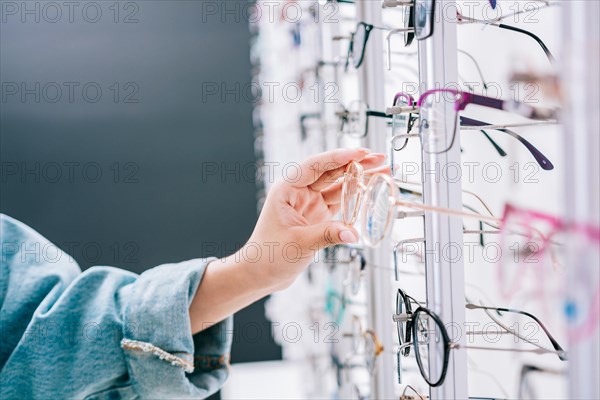 Girl hands choosing glasses in a store. Female buyer choosing glasses in a store. Female customer choosing glasses in an optical store