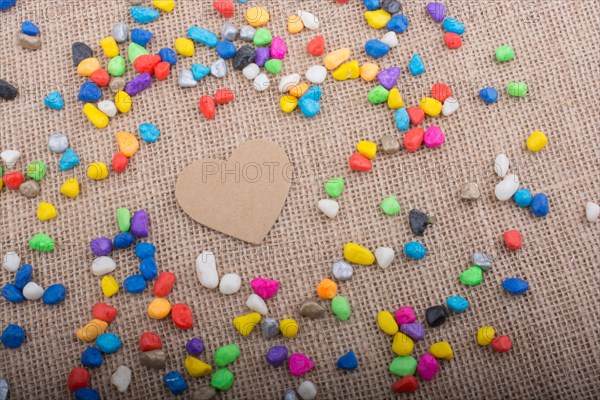 Paper heart amid colorful pebbles on canvas ground