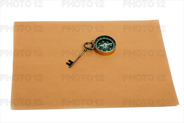 Key and compass on a sheet of colored plain paper with a white background