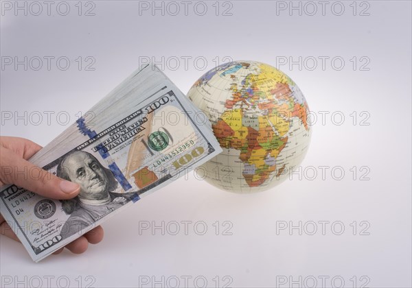 Human hand holding American dollar banknotes by the side of a model globe on white background