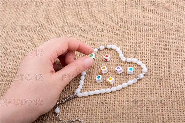 Heart shaped object in hand by a praying beads on canvas