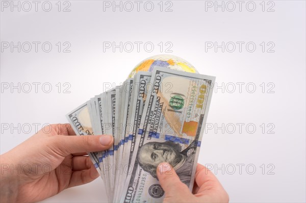 Human hand holding American dollar banknotes by the side of a model globe on white background