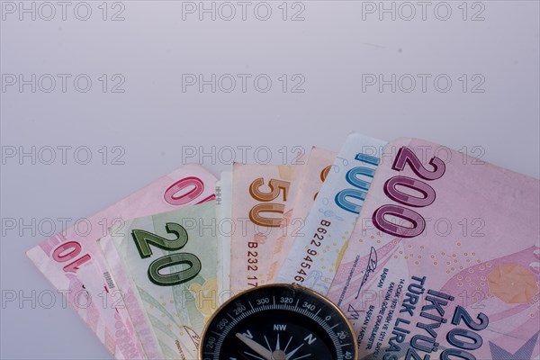 Turkish Lira banknotes by the side of a compass on white background
