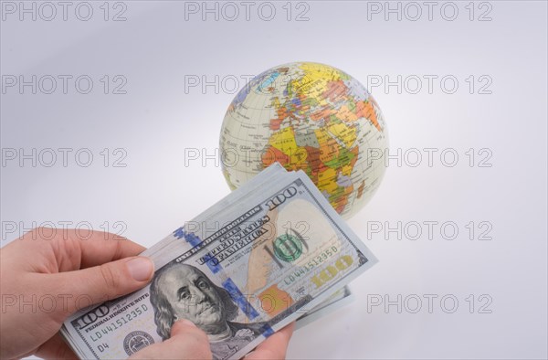 Human hand holding American dollar banknotes by the side of a model globe on white background