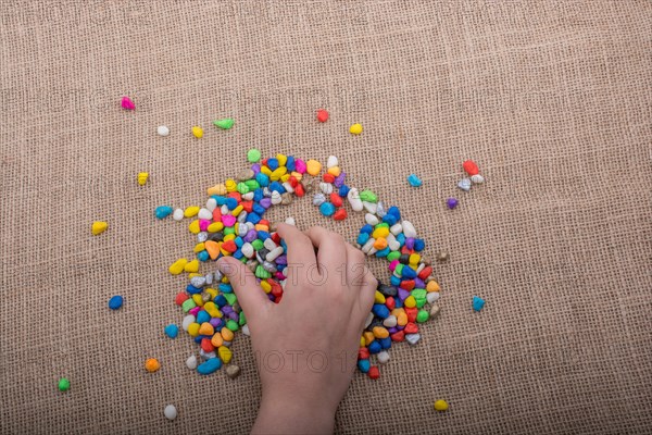 Colorful little pebbles in hand and on canvas ground