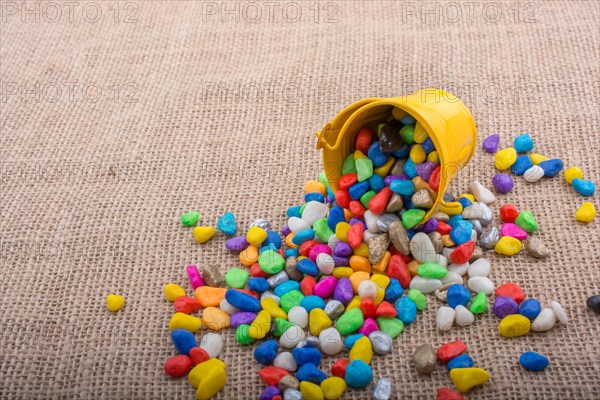 Bucket of colorful pebbles spill on background