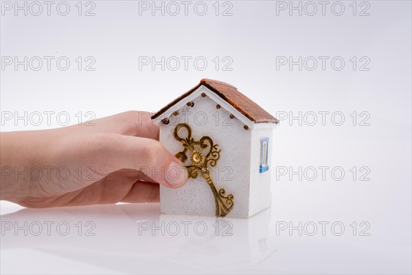 Hand holding a golden key near a house on a white background