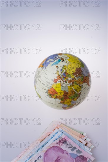 Turkish Lira banknotes by the side of a model globe on white background