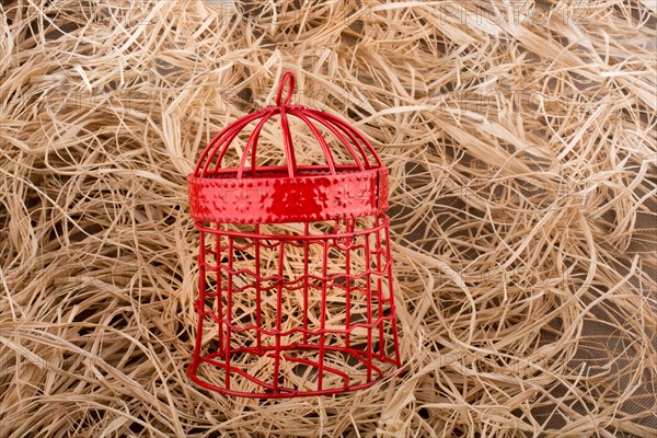 Red color bird cage placed on a straw background