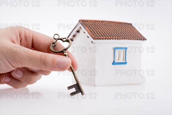 Hand holding a golden key near a house on a white background