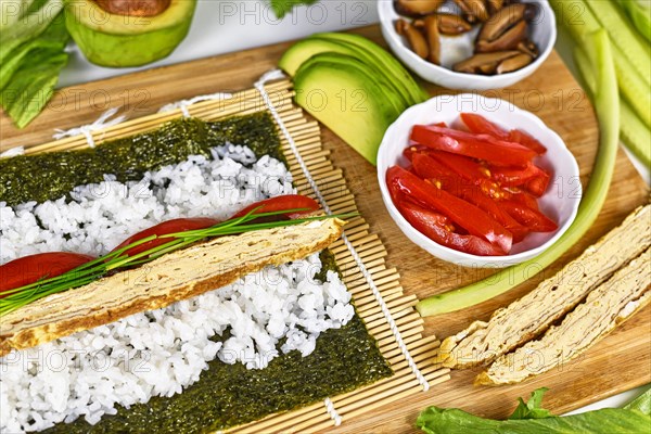 Preparing homemade vegetarian sushi with Nori algea sheet with rice on bamboo mat and ingredients like egg omelet