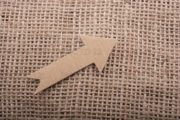 Arrow sign cut out of brown paper on canvas