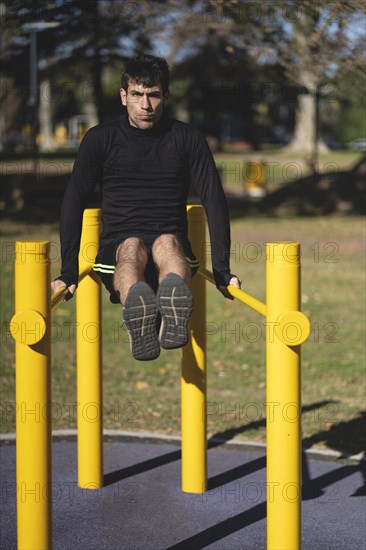 Fit young man doing push ups on horizontal bar outdoors