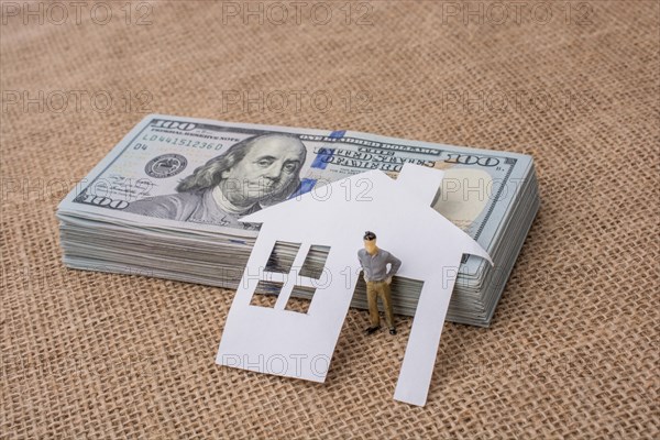 Paper house and a man figurine beside a bundle of US dollar banknote