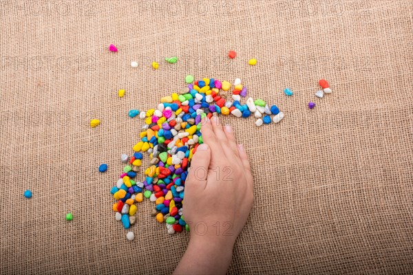 Colorful little pebbles in hand and on canvas ground