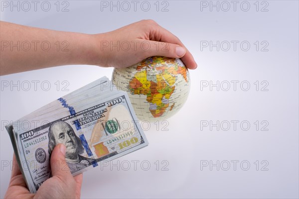 Human hand holding American dollar banknotes by the side of a model globe on white background