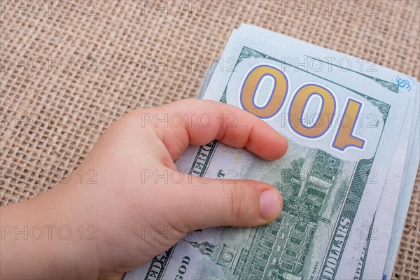 Toddler hand holding banknote bundle of US dollar on a linen canvas background