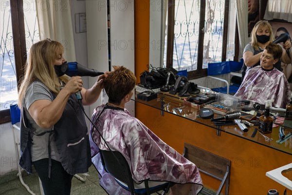 Latin hairdresser. Hairdresser blow-dries his client's hair. General shot