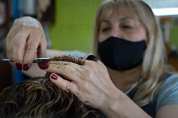 Woman with facemask cutting the hair with scissors and comb. Background blurred