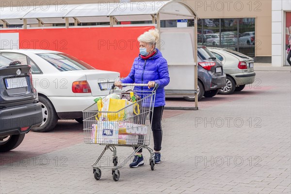 Shot of mature woman wearing protective mask with shopping cart on the parking lot during coronavirus pandemic. Everyday life