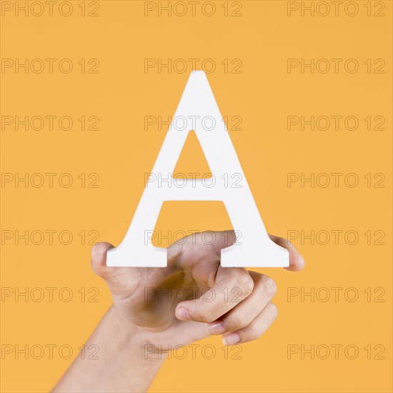 Human hand holding up uppercase capital letter yellow background