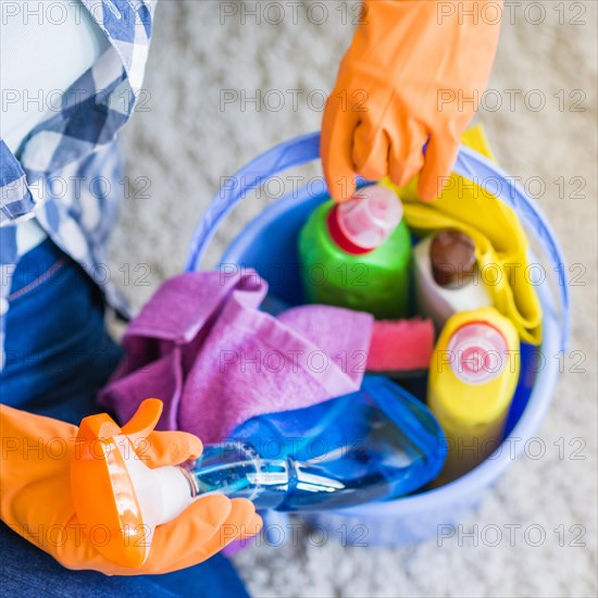 Woman removing cleaner spray bottle from blue bucket