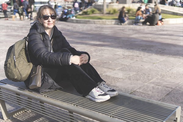 Mature woman sitting on a bench in the street at sunset with a relaxed and contemplative attitude