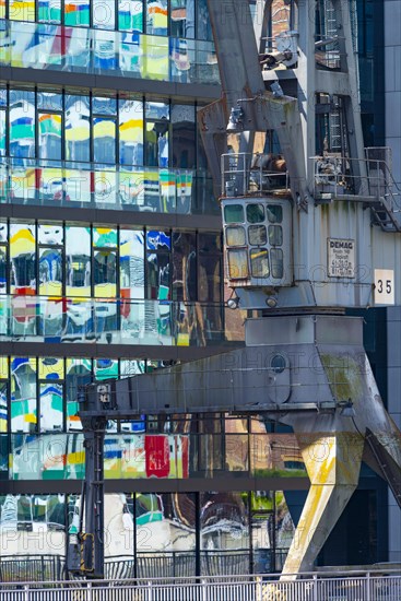 Old cargo crane in front of the glass facade of an office building