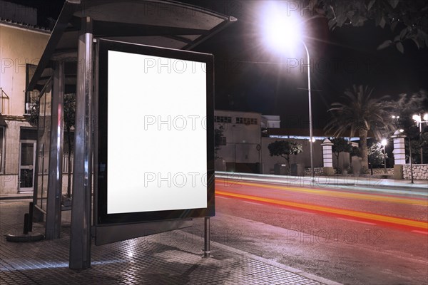 Blank advertisement bus shelter with blurred traffic lights night
