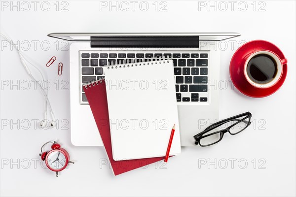 Overhead view office supplies laptop coffee cup alarm clock spectacles white desk