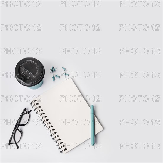 Overhead view disposable coffee cup push pins pen eyeglasses spiral notepad white background