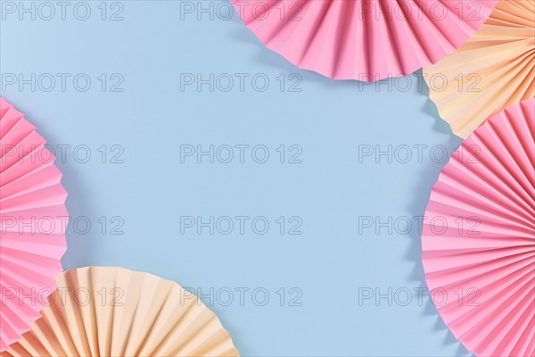 Beige and pink paper craft rosettes in corners of blue background with empty copy space in middle