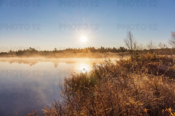Sun shining over a lake with morning fog at the lakeshore in autumn