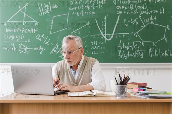 Old teacher using laptop classroom