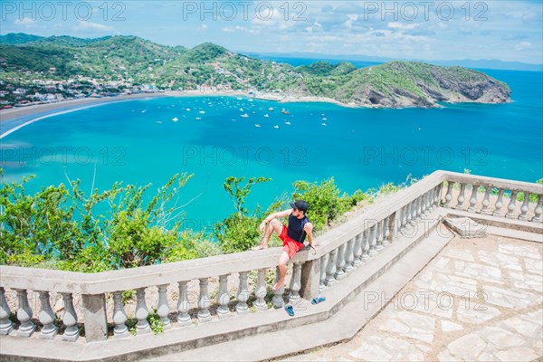 Happy tourist sitting in a viewpoint of a bay. Portrait of tourist man in the view of the bay of San Juan del Sur. Travel and tourism promotion concept