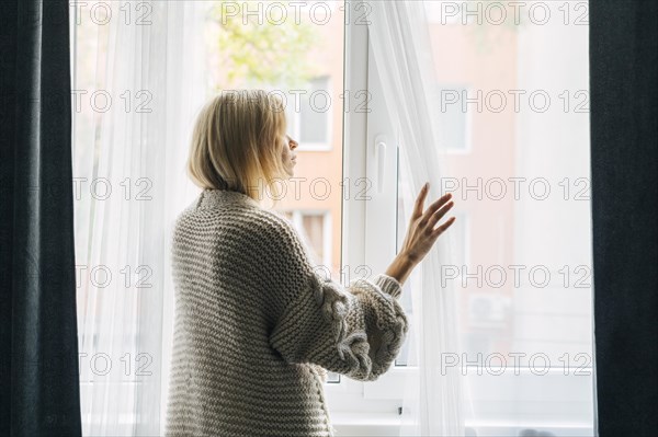 Side view melancholic woman home during pandemic looking through window