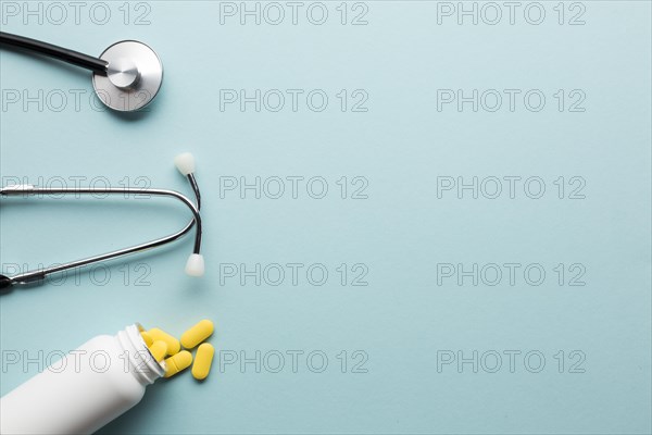 Yellow pills spilling out from white bottle near stethoscope blue surface