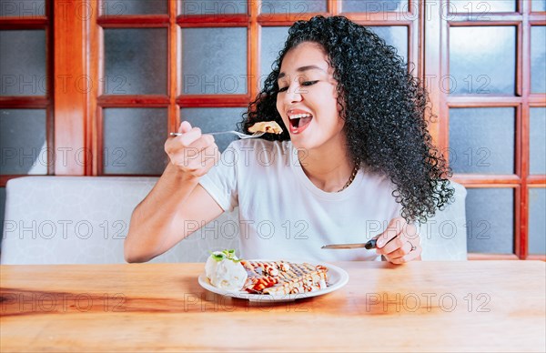 Beautiful girl eating chocolate crepe and ice cream with a fork. Hungry woman sitting eating chocolate crepe and ice cream