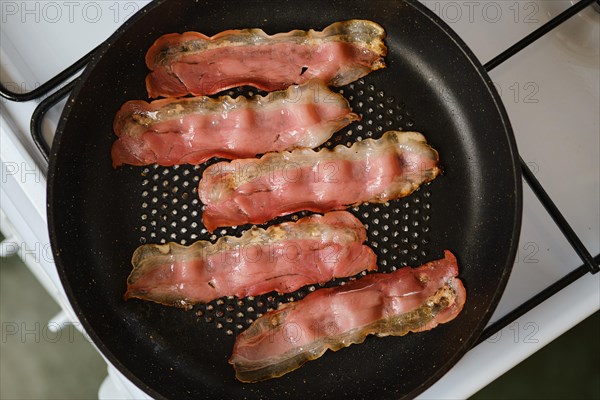 Frying bacon in a frying pan at home