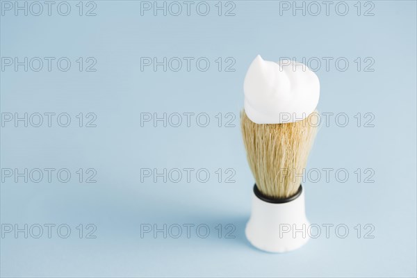 Overhead view classic shaving brush with white foam against blue background